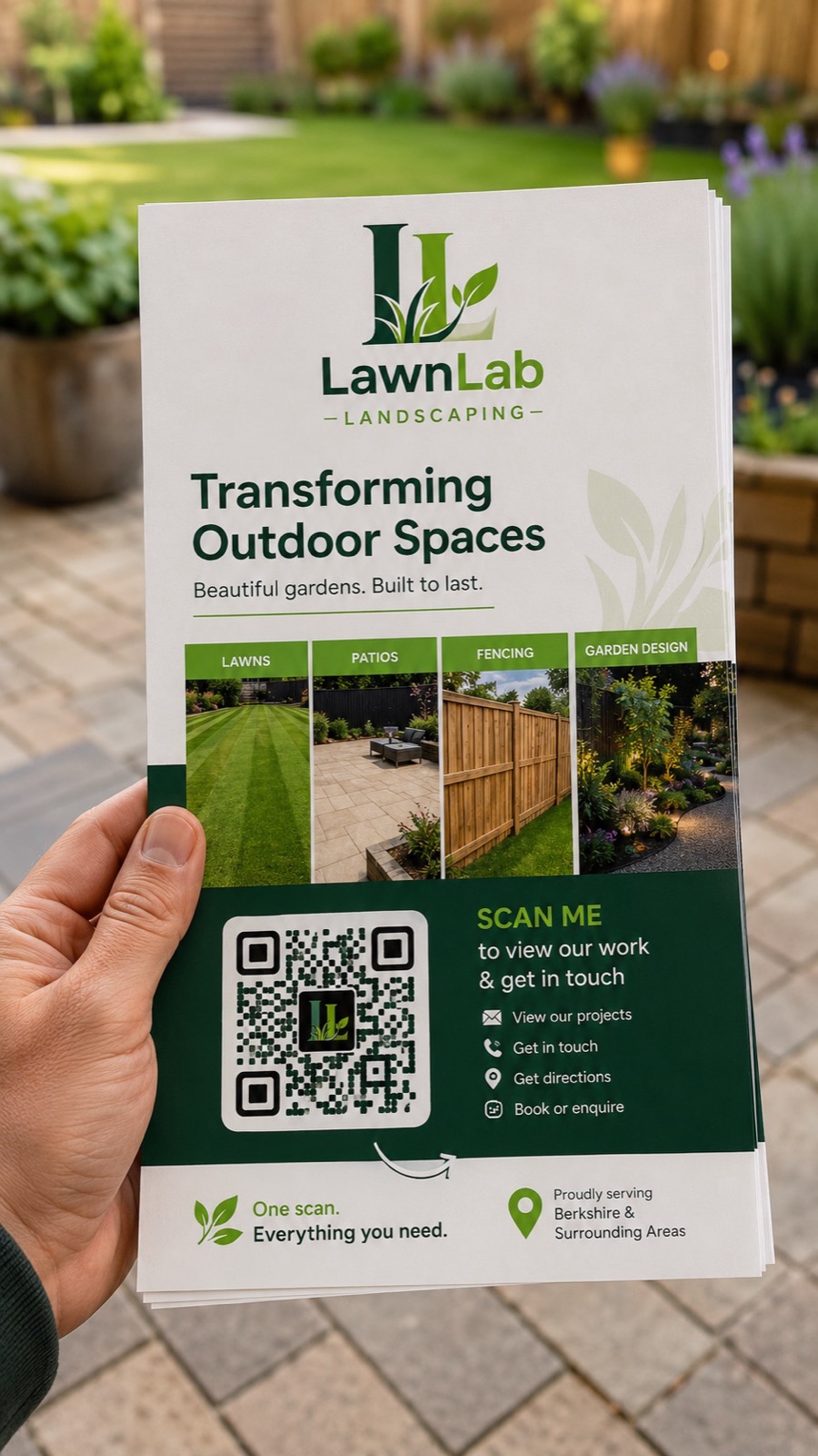 A hand holding a landscaping leaflet in a garden, a QR code with scan me to view our work and get in touch.